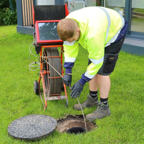 A drain cleaner working on a blocked drain via a manhole cover in a garden