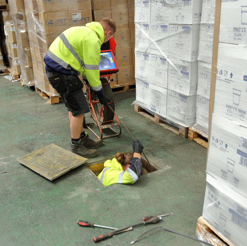 Two drain consultants working on a blocked drain in a warehouse