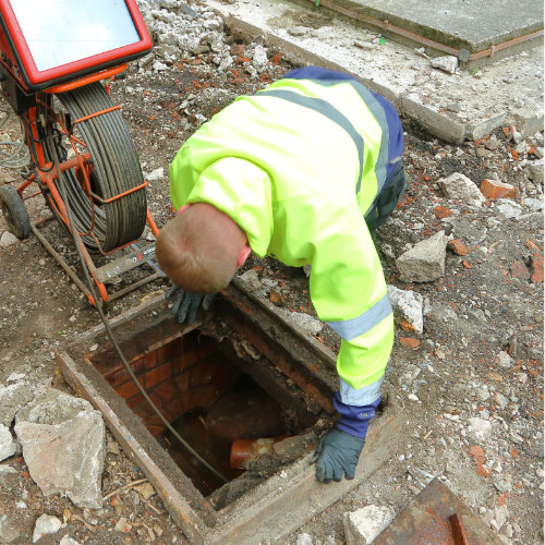 A drainage specialist inspecting a drain unblocking project using a manhole cover