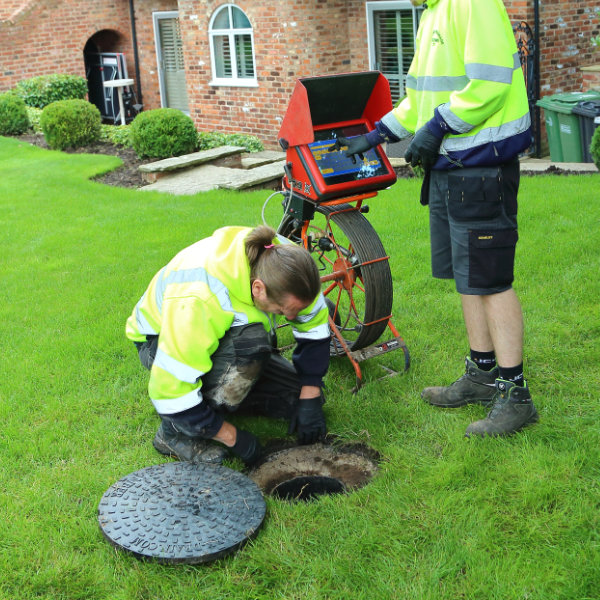 Two drainage experts starting a drain unblocking project in a garden of a house